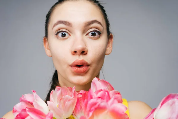 Mooi verrast meisje kijkend naar de camera, houden van roze bloemen — Stockfoto