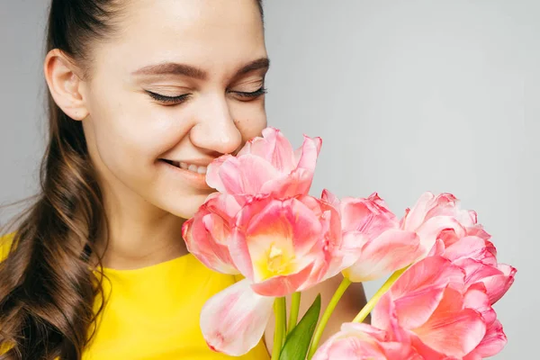 Charming smiling girl in a yellow dress smelling beautiful pink flowers — Stock Photo, Image