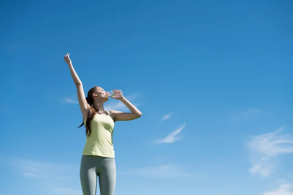 Aktivní štíhlá holka pije vodu po těžké cvičení, pod modrou oblohou — Stock fotografie