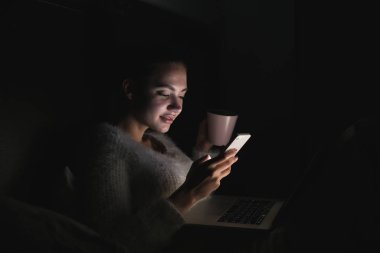 Genç kız yatakta gece geç saatlerde, bir film seyrederken onu laptop telefonda mesaj yazarken oturmuş