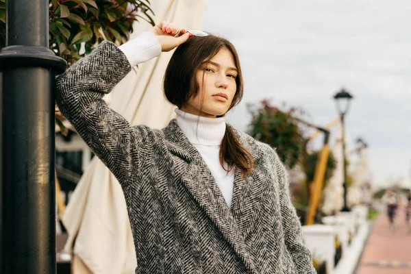 Confident stylish brunette girl in a trendy gray coat walking through the streets of the city and posing — Stock Photo, Image