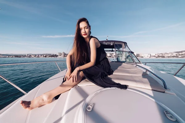 Una chica de lujo en ropa negra se sienta en su yate blanco, disfruta de unas vacaciones —  Fotos de Stock