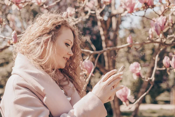 Hermosa mujer rizada disfruta de una fragante magnolia rosa, sonriendo — Foto de Stock