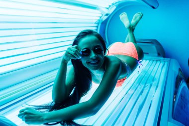 ince kız gözlük, ultraviyole ışınları altında bir bronzlaşma yatakta esmer güneşlenme gülümseyen