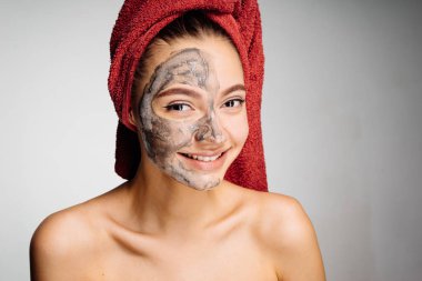 güzel genç kız başında kırmızı bir havlu ile uygulanan bir kil maskesi yarım yüz, Spa gün