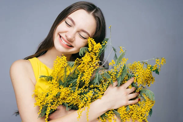 Beautiful young girl smiling, enjoying the spring, holding a big bouquet of fragrant yellow mimosa — Stock Photo, Image