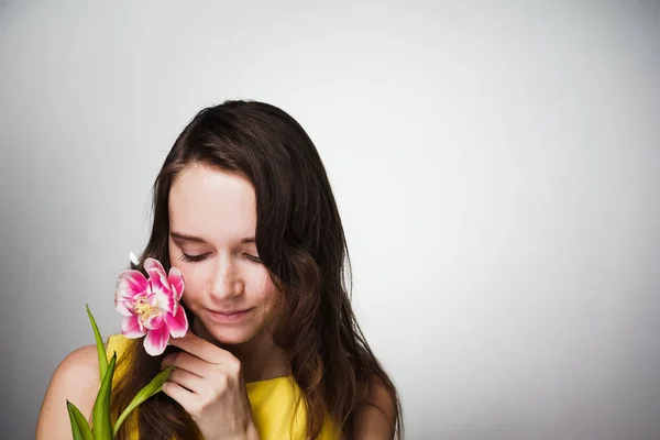 Charmante schöne Mädchen in gelbem Kleid hält duftende rosa Blume, posiert — Stockfoto