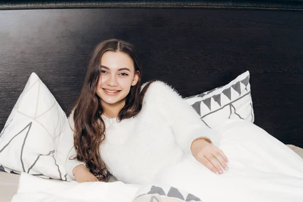 Joven somnolienta con el pelo largo se encuentra en la cama, sonríe y quiere dormir — Foto de Stock