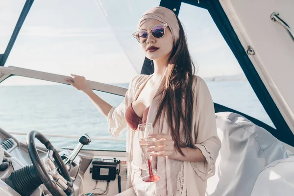An elegant young woman in sunglasses runs her yacht, enjoys a vacation on the sea — Stock Photo, Image