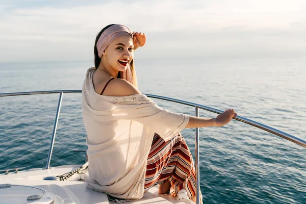 Hermosa mujer sonriente en ropa de verano con estilo sentado en un yate blanco, disfrutando de la calidez y el sol —  Fotos de Stock