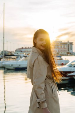 gün batımı ve deniz, karşı poz trendy paltolu güzel uzun saçlı kız gülümseyerek