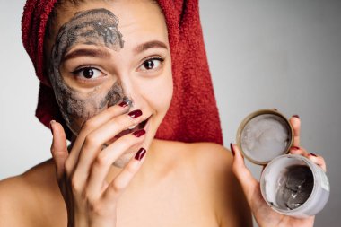 başında kırmızı bir havlu ile genç kız yüzünü yararlı kil maskesi koyar.