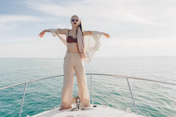 Una joven con estilo en ropa de verano está de pie en un yate, disfrutando del cálido viento del verano y el sol —  Fotos de Stock