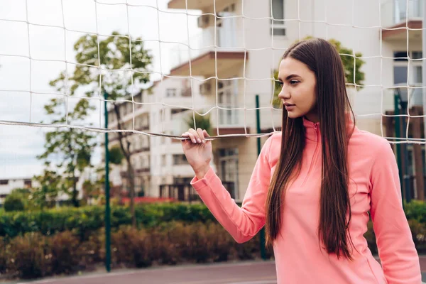 Confident long-haired girl likes to play volleyball, stands on the sports field at the net — Stock Photo, Image