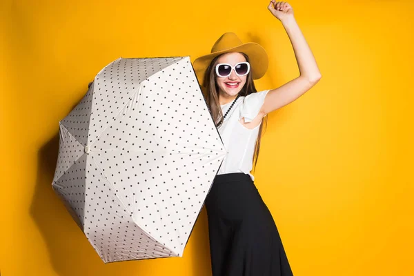 Elegante bella ragazza modello in occhiali da sole e cappello tiene ombrello, in posa su sfondo giallo — Foto Stock