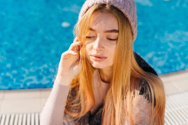 Giovane ragazza bionda carina in un cappello rosa a riposo presso la piscina blu, godendo il calore — Foto Stock