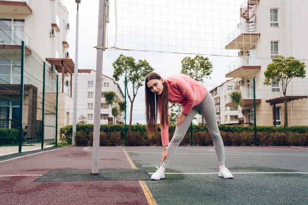 Activa chica de pelo largo en una chaqueta rosa se extiende antes del entrenamiento, quiere perder peso — Foto de Stock