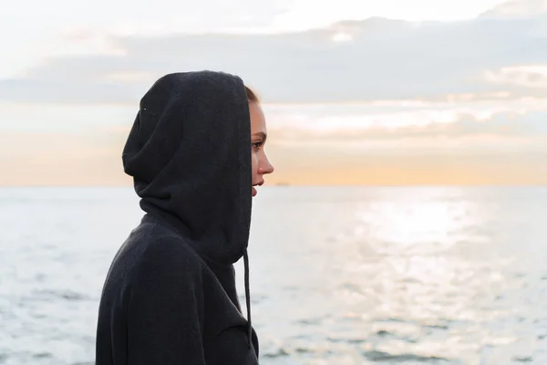 Uma jovem com um capuz na cabeça desfrutando da manhã e da vista para o mar — Fotografia de Stock