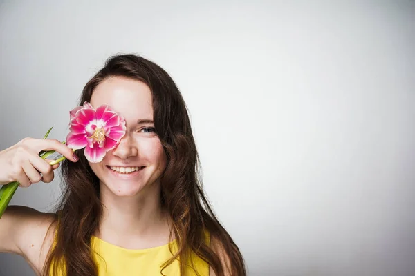 Encantadora chica sonriente en vestido amarillo está sosteniendo flor rosa cerca de la cara, posando — Foto de Stock