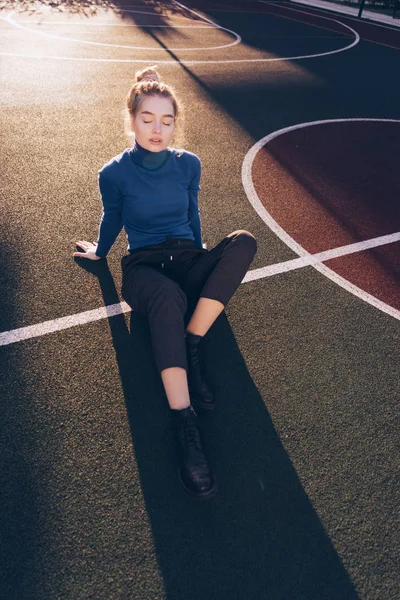 Jovem menina loira elegante em suéter azul posando no campo de esportes no sol da manhã — Fotografia de Stock