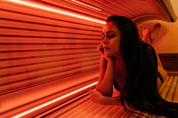 Mooi donker-haired meisje ligt in het solarium, zonnen onder de ultraviolette stralen — Stockfoto