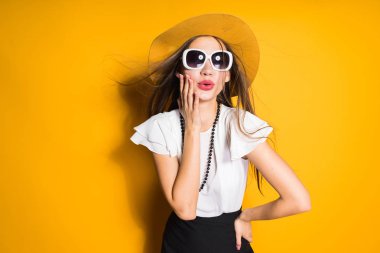 Lüks uzun saçlı kız moda şapka ve güneş gözlüğü sarı bir arka plan üzerinde poz