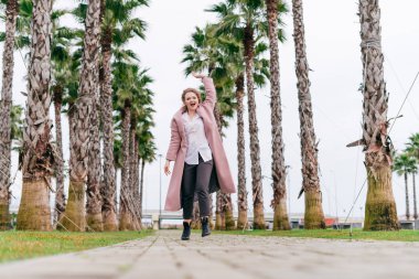 pembe bir ceket etkin neşeli kadın bahar parkta yürüyor, sıcaklık sahiptir