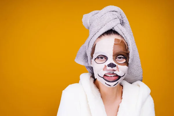 Legrační mladá dívka v bílém plášti, ručník na hlavě, hydratační maska s psí tvář na tvář — Stock fotografie