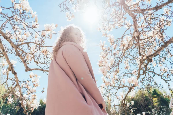 Stylish girl in a trendy pink coat posing under a blue sky in a park, enjoying the warmth — Stock Photo, Image