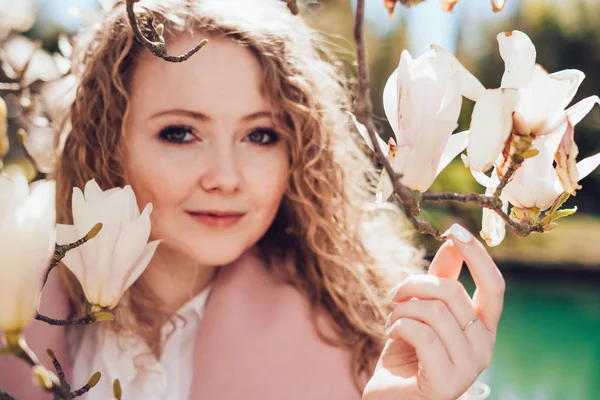 Bouclé belle femme profiter de l'odeur d'un magnolia en fleurs dans un parc, posant — Photo