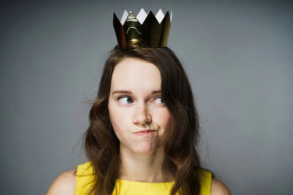Una joven seria con un vestido amarillo pensó en algo importante, una corona dorada en su cabeza — Foto de Stock