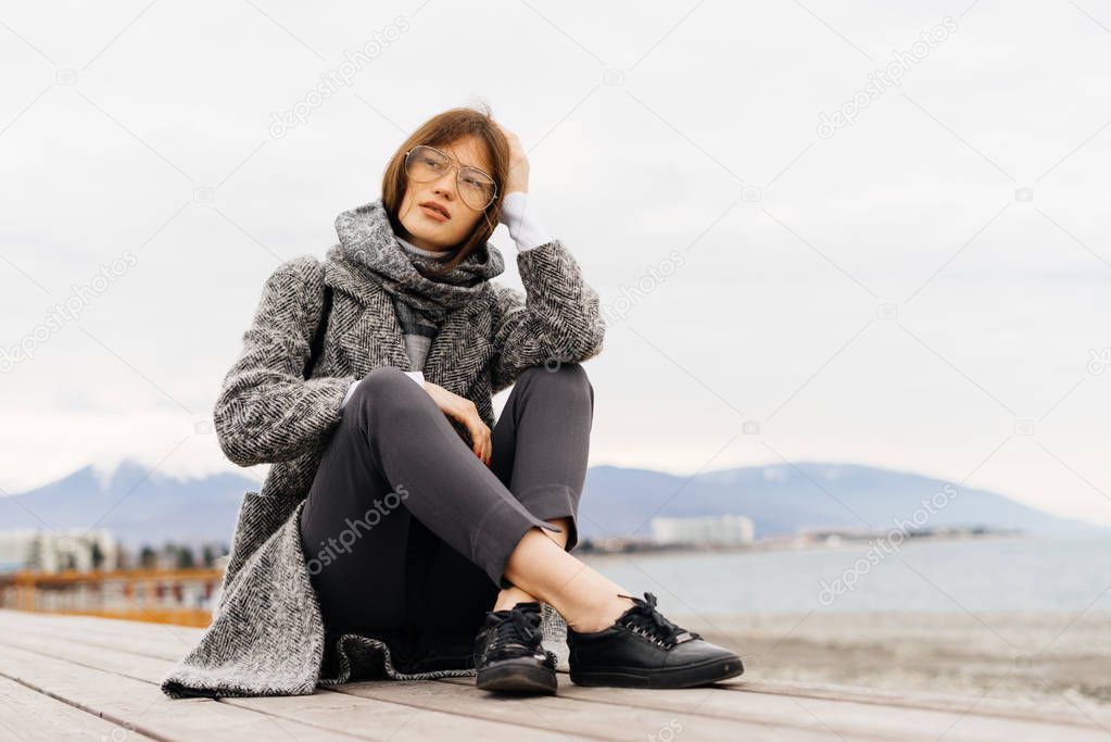 stylish young brunette girl in spectacles enjoying the sea view, cloudy weather