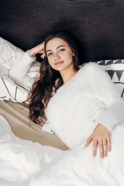 Joven chica bonita se despertó temprano en la mañana, se encuentra en su cama, en casa, sonriendo — Foto de Stock