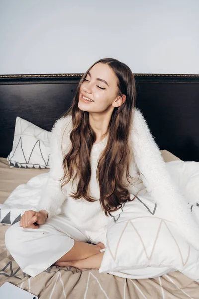 Elegáns lány, szép hosszú haja ül az ágyon, reggel ébredt fel egy jó hangulatban, mosolyogva — Stock Fotó