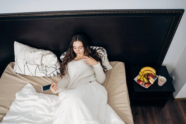 Joven se encuentra debajo de una manta blanca en la cama por la noche, descansando y quiere dormir — Foto de Stock