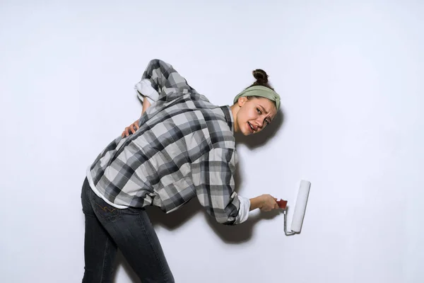Уставшая молодая девушка красит стены в белое роликом, повреждает спину — стоковое фото