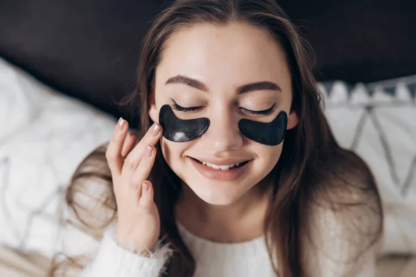 Affascinante bella ragazza si siede sul letto, si sveglia presto la mattina e sorride, sotto gli occhi macchie nere — Foto Stock