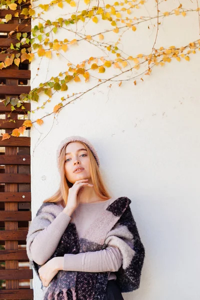 Молода блакитноока дівчина блондинка в теплому стильному одязі позує на стіну в постріл на сонці — стокове фото