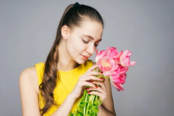 Schattige mooie meisje in een gele jurk bedrijf een boeket van roze bloemen in haar handen, genieten van de geur — Stockfoto