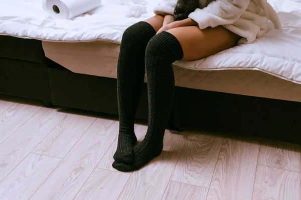 Slender girl in a white terry dressing gown and black golf sits on the bed — Stock Photo, Image