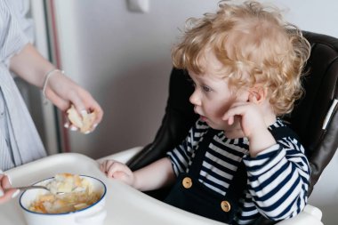 Mutfakta, lezzetli sıcak çorba besleme anne oturan küçük kıvırcık bebek çocuk