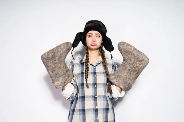 Divertida chica rusa con coletas en un sombrero negro cálido sostiene botas de fieltro gris, espera el invierno — Foto de Stock