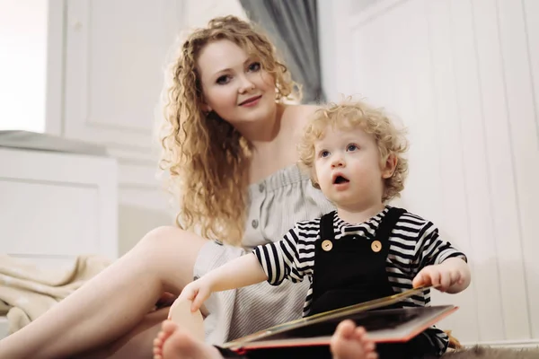 Curly young mother sitting on the floor next to her son, having fun together — Stock Photo, Image