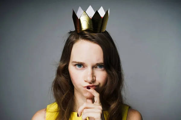 Menina séria em um vestido amarelo pensa em algo, em sua cabeça uma coroa de ouro — Fotografia de Stock