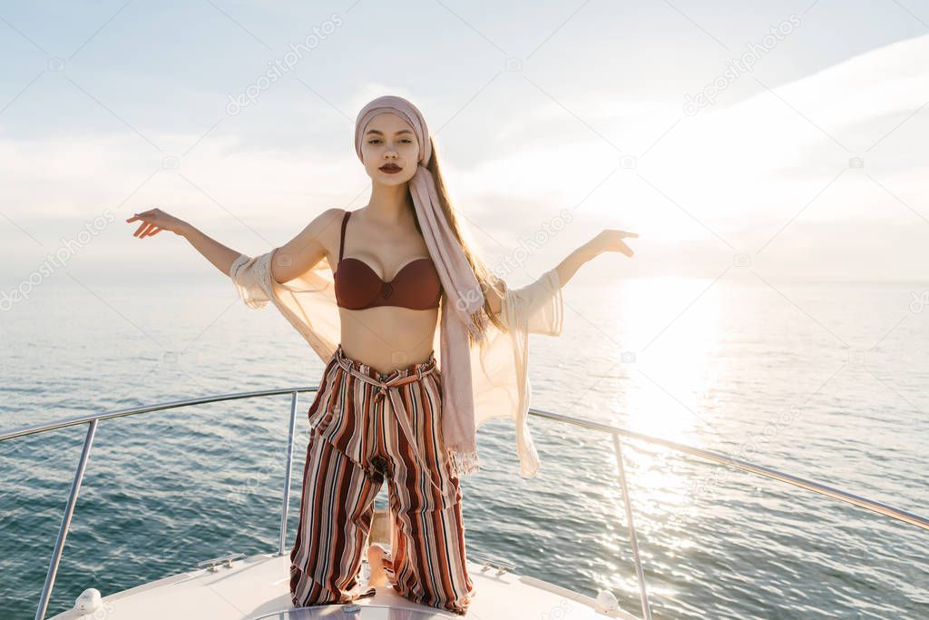a beautiful stylish girl in fashionable summer clothes rests and relaxes in the rays of the summer sun, sails on the sea