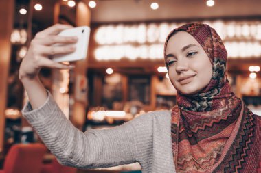 hijab büyüleyici Arap kız selfie onu Smartphone'da yapar, rahat bir restoranda oturur
