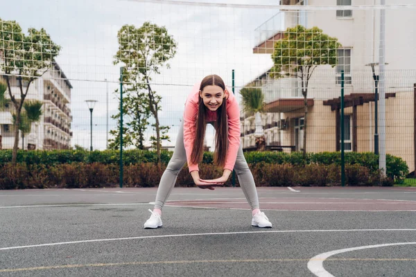 Chica atlética de confianza con el pelo largo calentado y estirado antes de entrenar en el campo de deportes — Foto de Stock