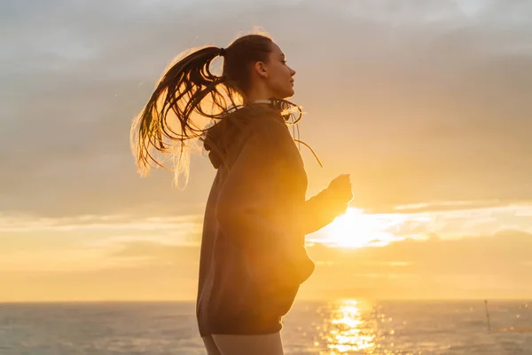 Dai capelli lunghi ragazza veloce jogging lungo il lungomare al tramonto, vuole perdere peso — Foto Stock