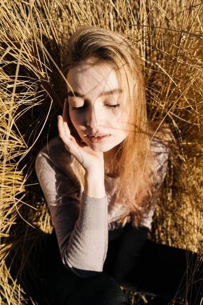 Encantadora menina loira confiante descansando na grama ao sol, apreciando o calor e posando — Fotografia de Stock