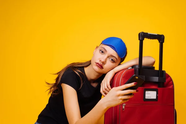 a tired young girl rests on her red suitcase, waits long for her plane, wants to leave
